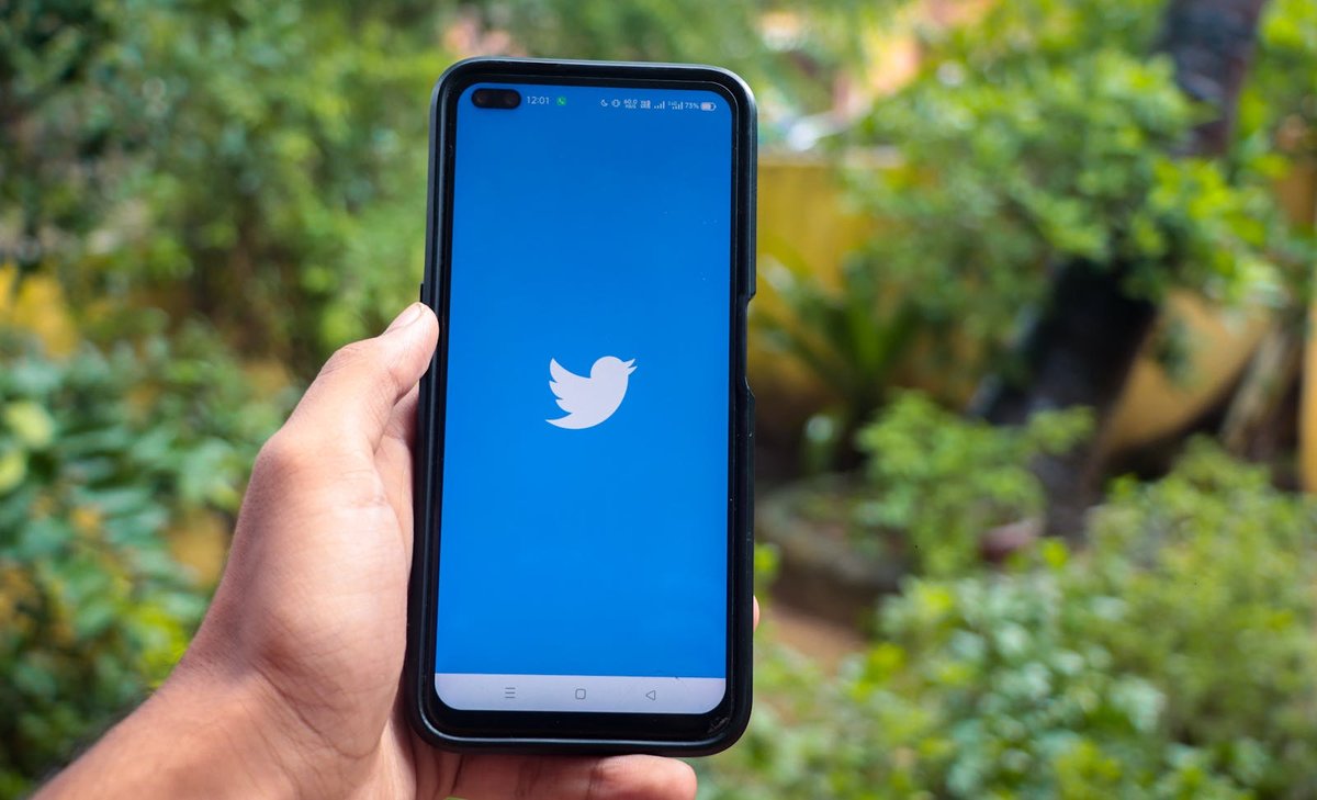 Hand holding a smartphone with the Twitter (X) app on screen